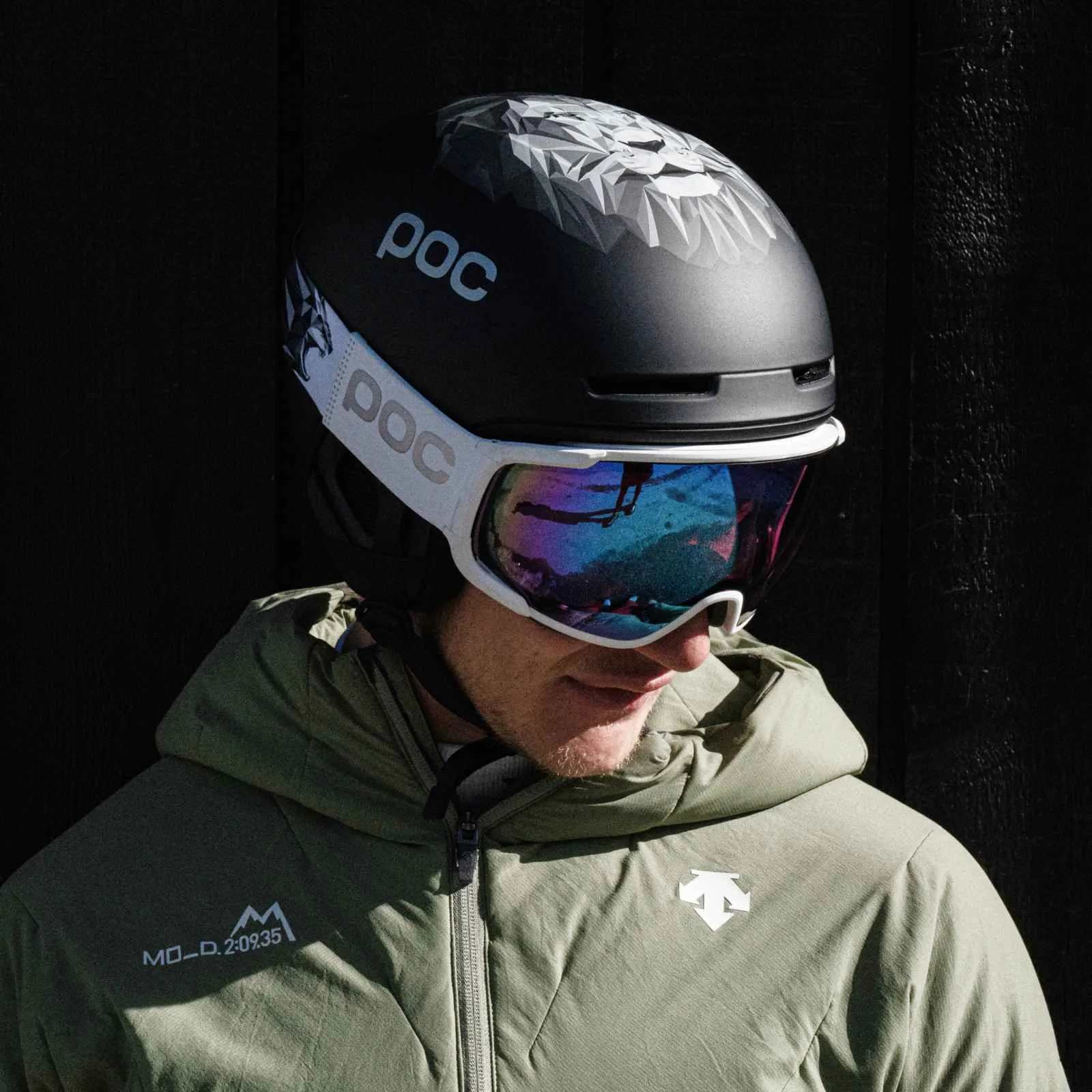 Mann mit POC Skihelm, Lwen-Motiv, und Skibrille. Reflektion in der Brille. Grüne Jacke.