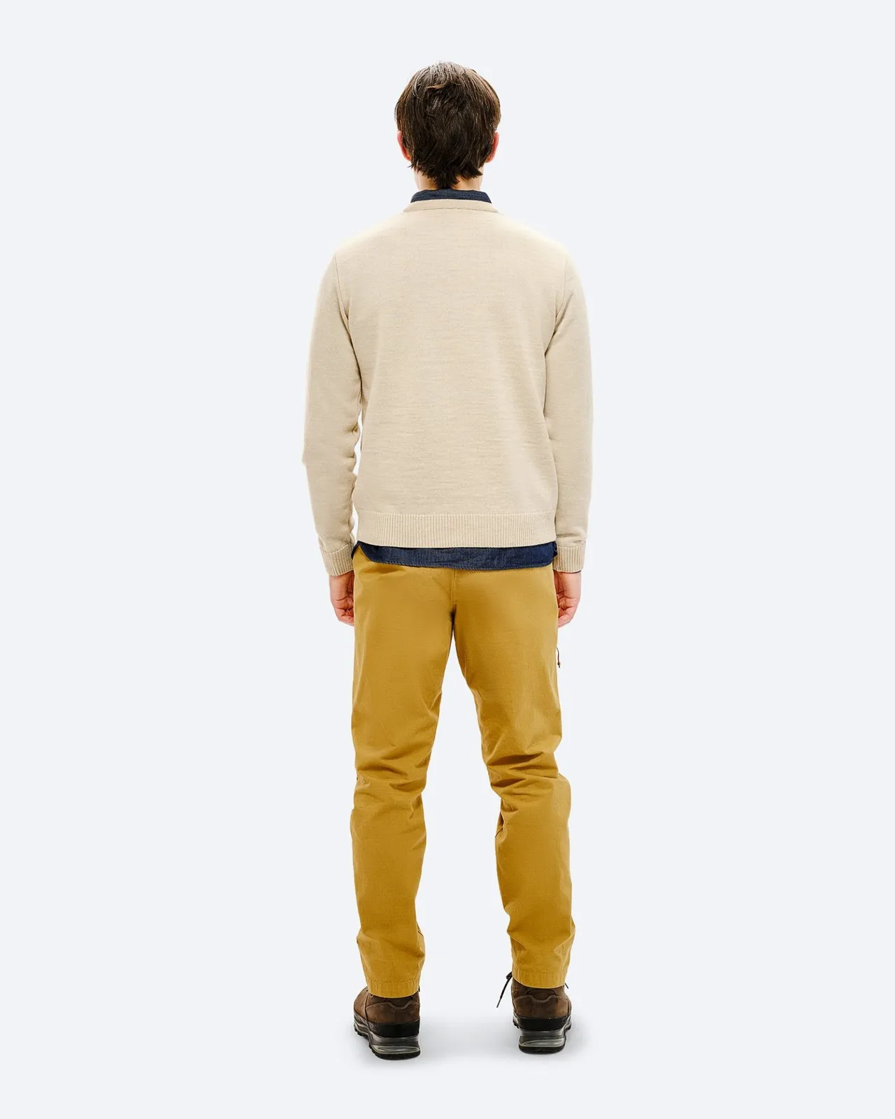 Rückansicht eines Mannes mit beigem Ski Sweater, gelben Hosen und braunen Schuhen vor neutralem Hintergrund.
