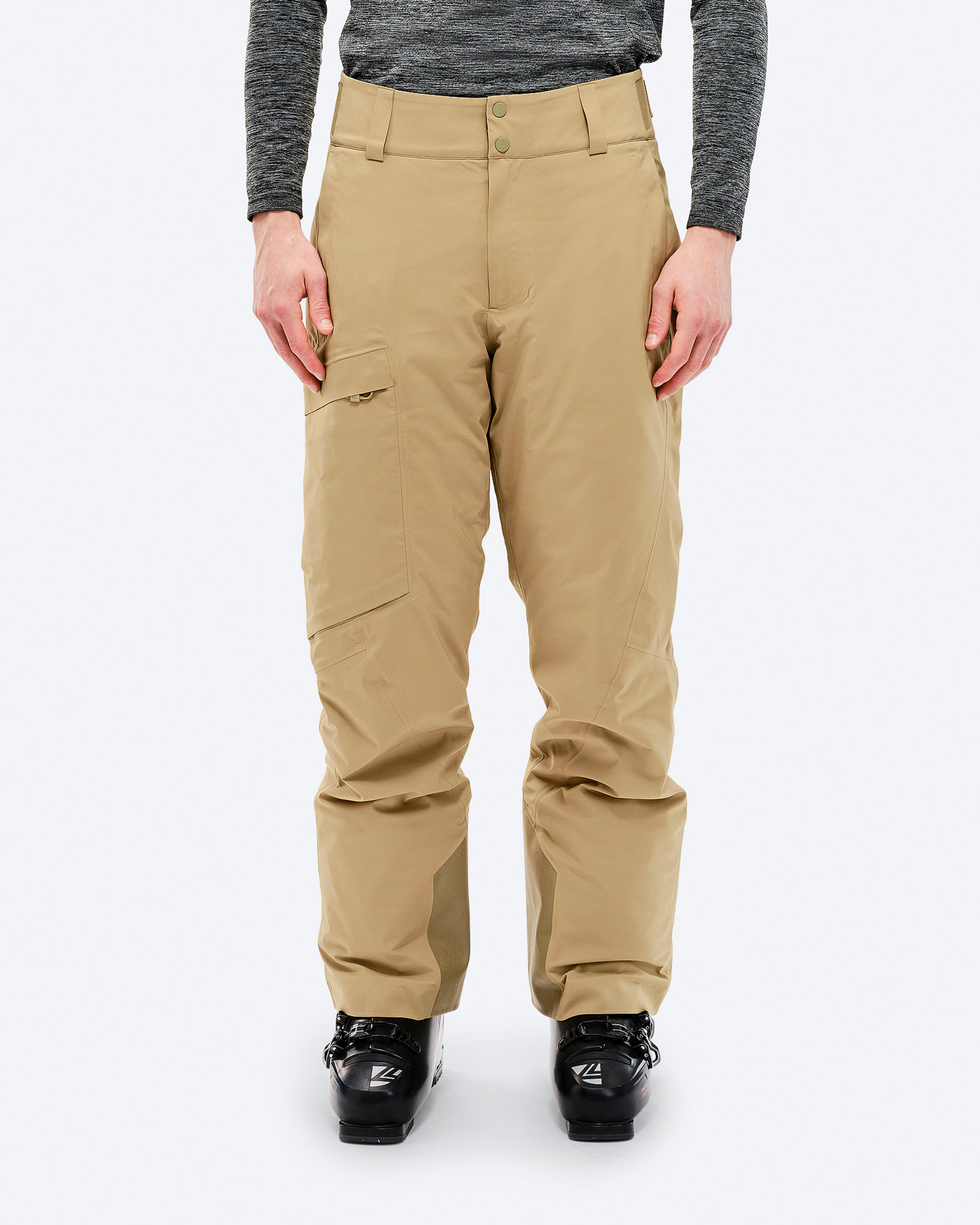 Eine Person trägt eine Sandfarbene P-1 GORE-TEX 2L Stretch Insulated Skihose und Skischuhe vor einem weißen Hintergrund.
