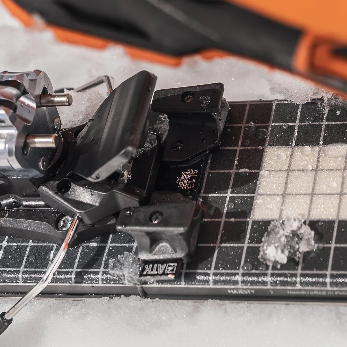 ATK Skitourenbindung Nahaufnahme Nahaufnahme einer Skitourenbindung von ATK auf einem Ski mit einem schwarz-weißen Schachbrettmuster. Schnee liegt auf dem Ski.