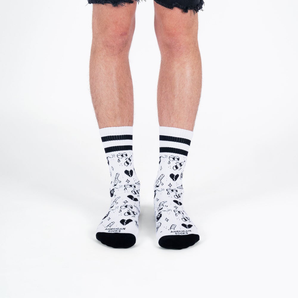 Beine mit weißen, mittelhohen Socken, verziert mit schwarzen Tattoo-Motiven und Streifen am oberen Rand.