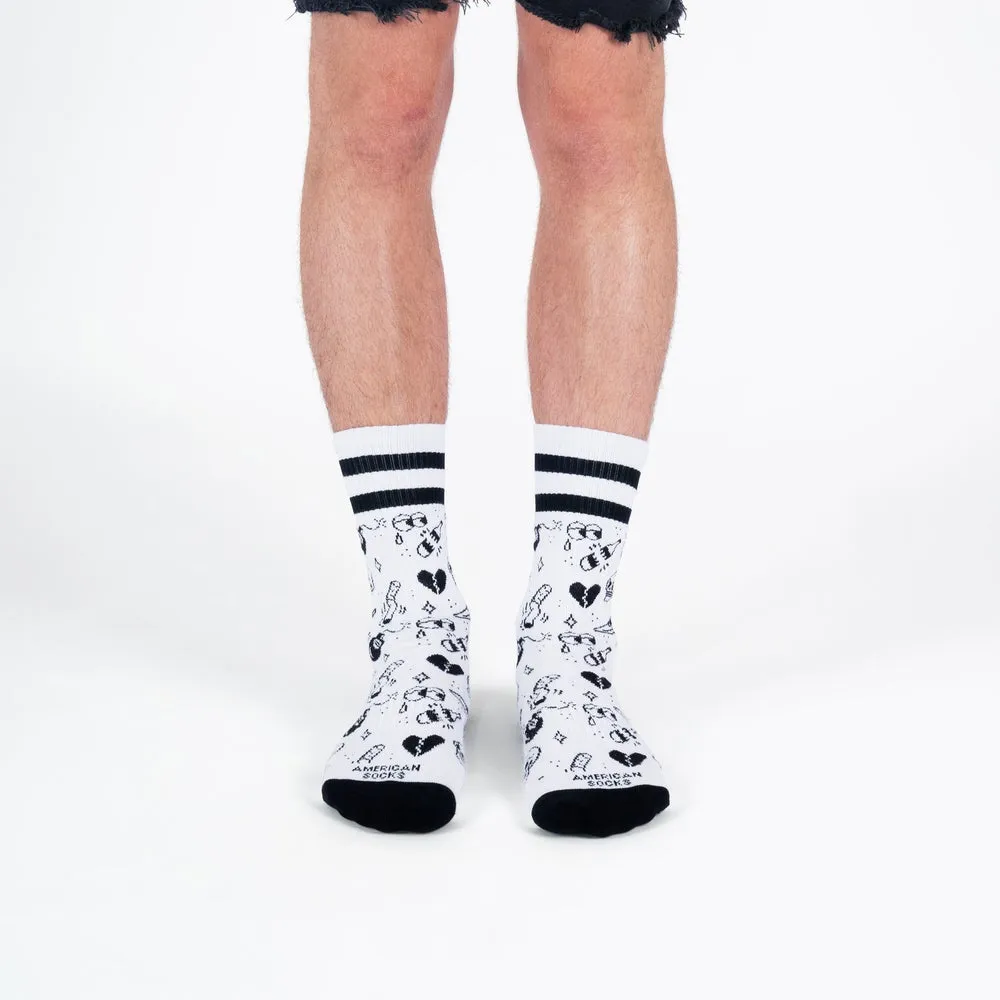 Beine mit weißen, mittelhohen Socken, verziert mit schwarzen Tattoo-Motiven und Streifen am oberen Rand.