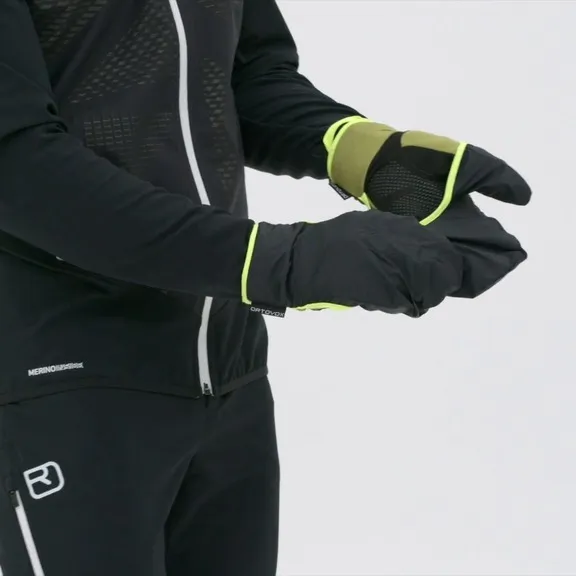 Eine Person trägt Ortovox Fleece Grid Cover Handschuhe in Schwarz und Grün. Der Cover Hoody ist über die Finger gezogen.