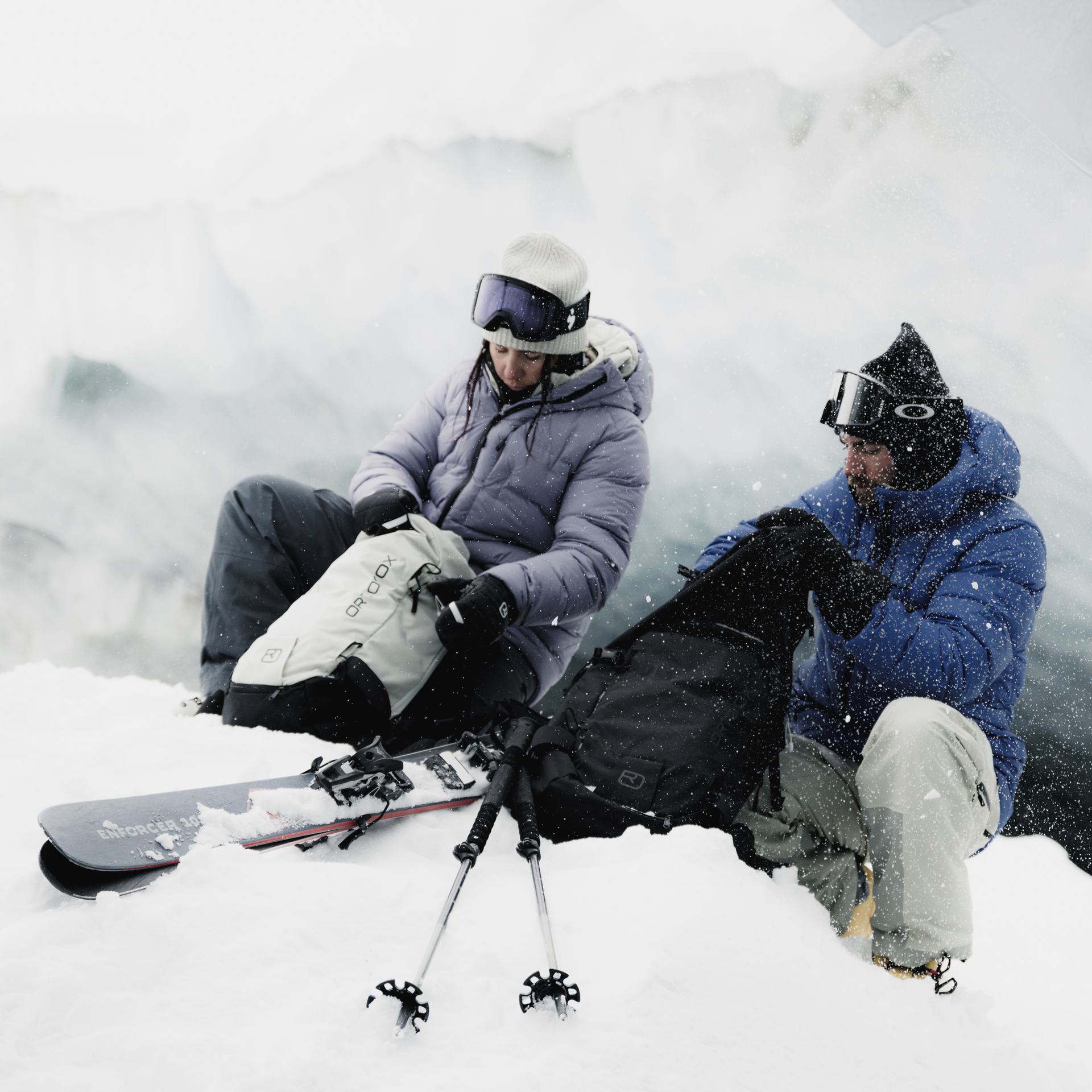 Skifahrer am Gletscher Zwei Skifahrer sitzen im Schnee vor einem Gletscher und öffnen ihre Rucksäcke. Skier und Stöcke liegen im Schnee.