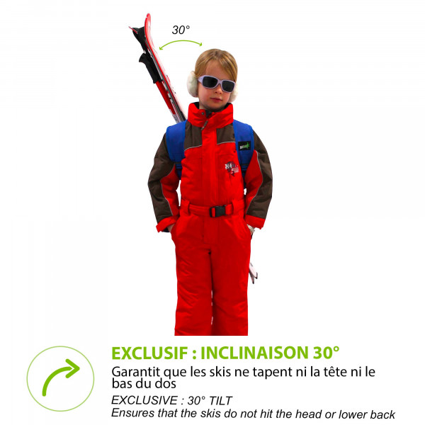 Kind mit Skiern auf dem Rücken mit Skiback Kids Blue. Roter Skianzug und Sonnenbrille. Ski ragen schräg nach oben.