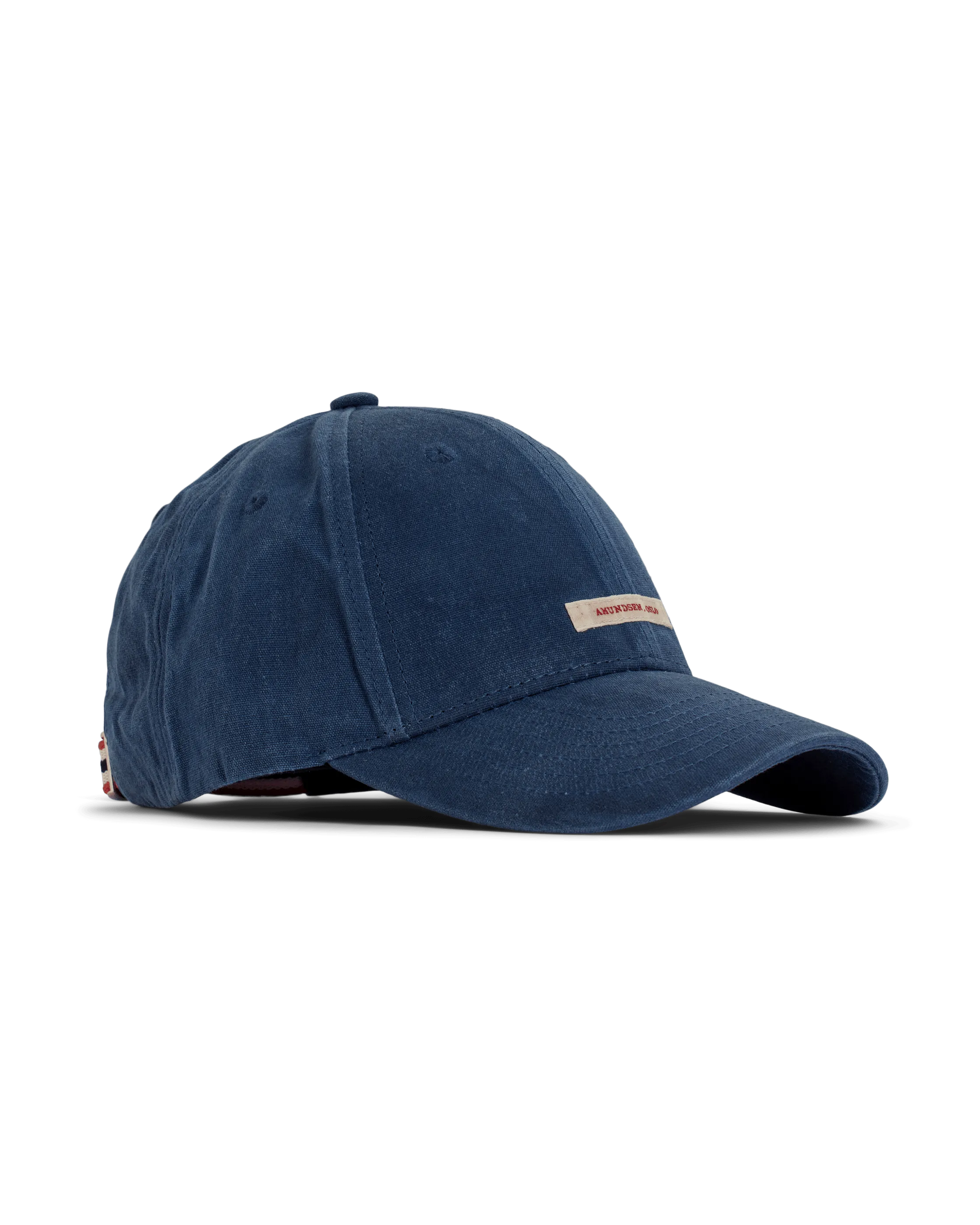 Eine dunkelblaue Amundsen Waxed Cotton Cap, auf weißem Grund, mit kleinem, beigefarbenem Logo über dem Schirm. Der Stoff der Kappe ist gewachst. Die Kappe ist auf der Seite fotografiert, so dass Form gut sichtbar ist.