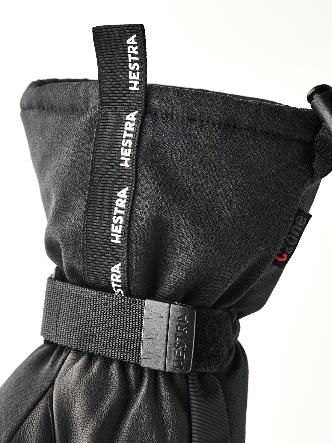 Nahaufnahme eines schwarzen Hestra-Handschuhs mit Zugband und verstellbarem Riemen.