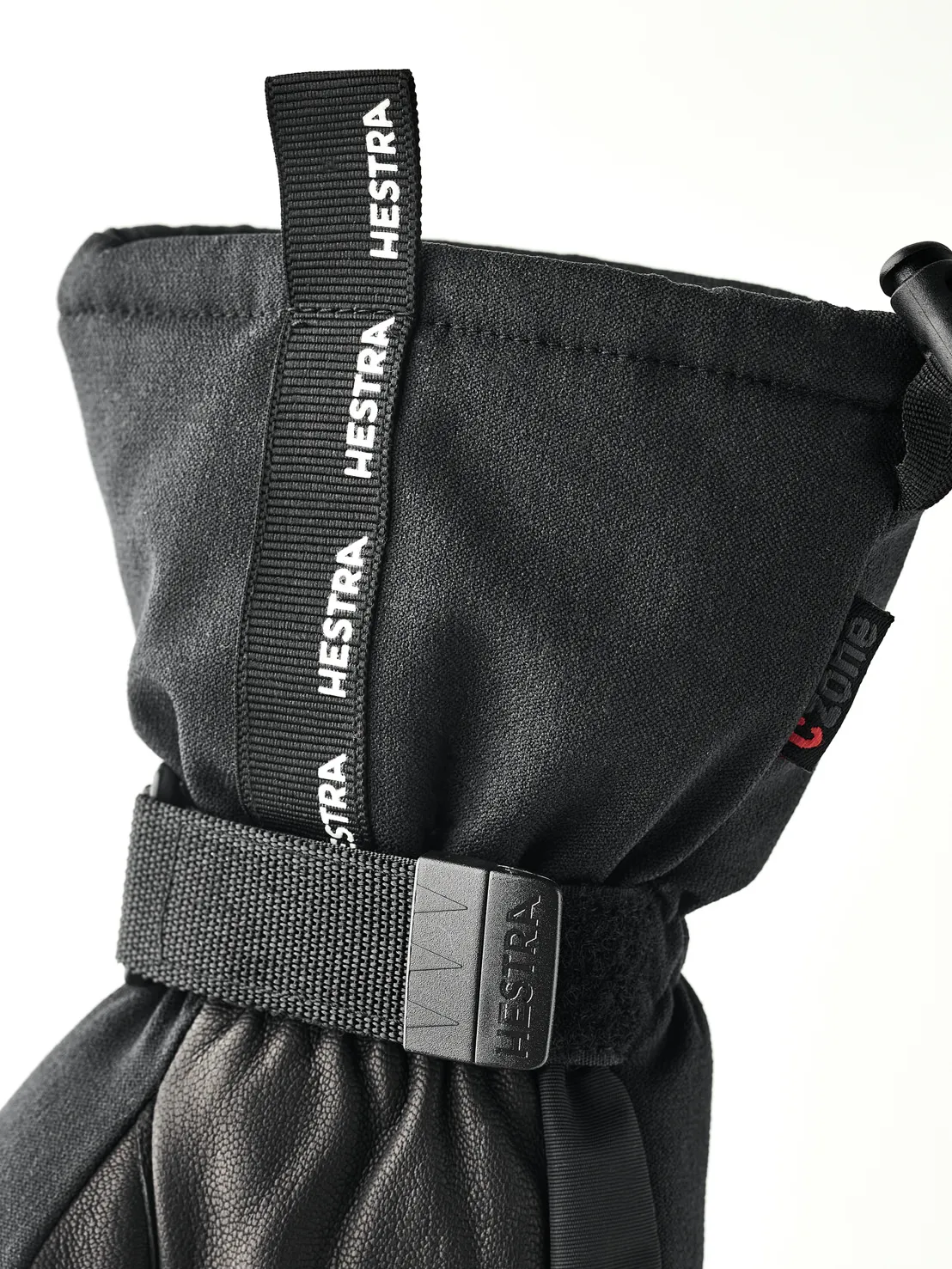 Nahaufnahme eines schwarzen Hestra-Handschuhs mit Zugband und verstellbarem Riemen.