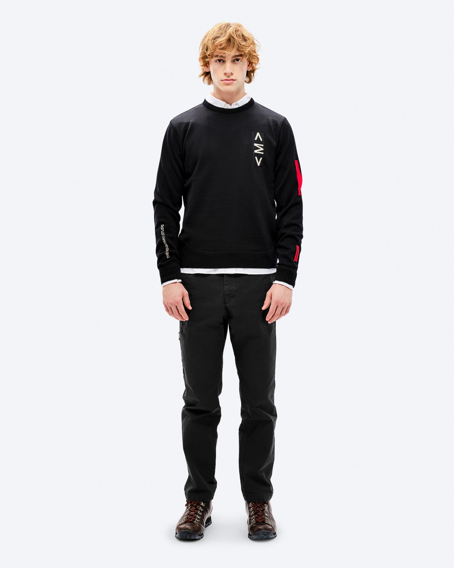 Mann mit rotem Haar trägt schwarzen K-3 Ski Sweater mit roten Akzenten und schwarzen Hosen, posiert vor einem weißen Hintergrund.