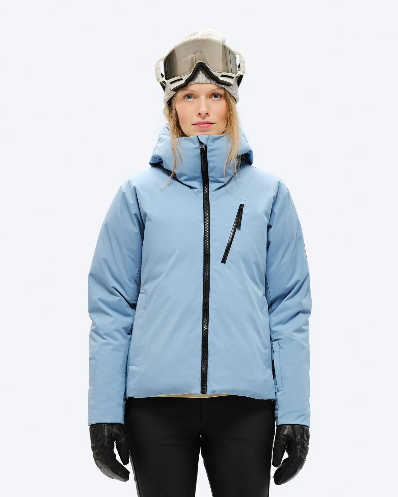 Eine Frau mit Mütze und Skibrille trägt eine hellblaue Daunenjacke mit Kapuze und schwarzem Reißverschluss.
