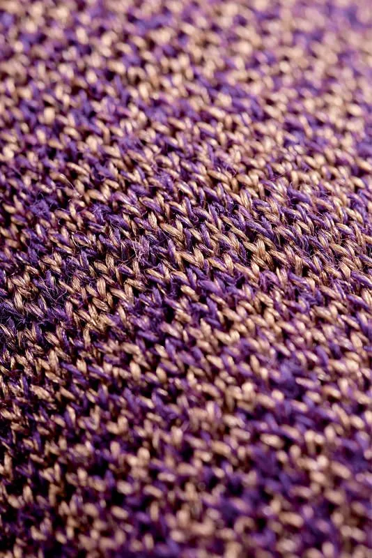 Nahaufnahme des Strickmusters einer Skisocke mit Merinowolle in Lila- und Beigetönen.