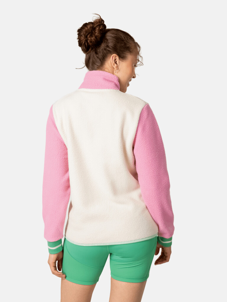 Rückansicht eines Models im Rothe Midlayer: Rosa Ärmel, cremefarbener Rumpf und grüne Shorts.