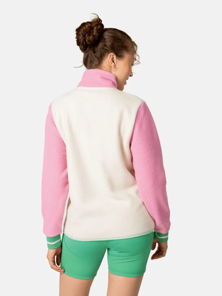 Rückansicht eines Models im Rothe Midlayer: Rosa Ärmel, cremefarbener Rumpf und grüne Shorts.