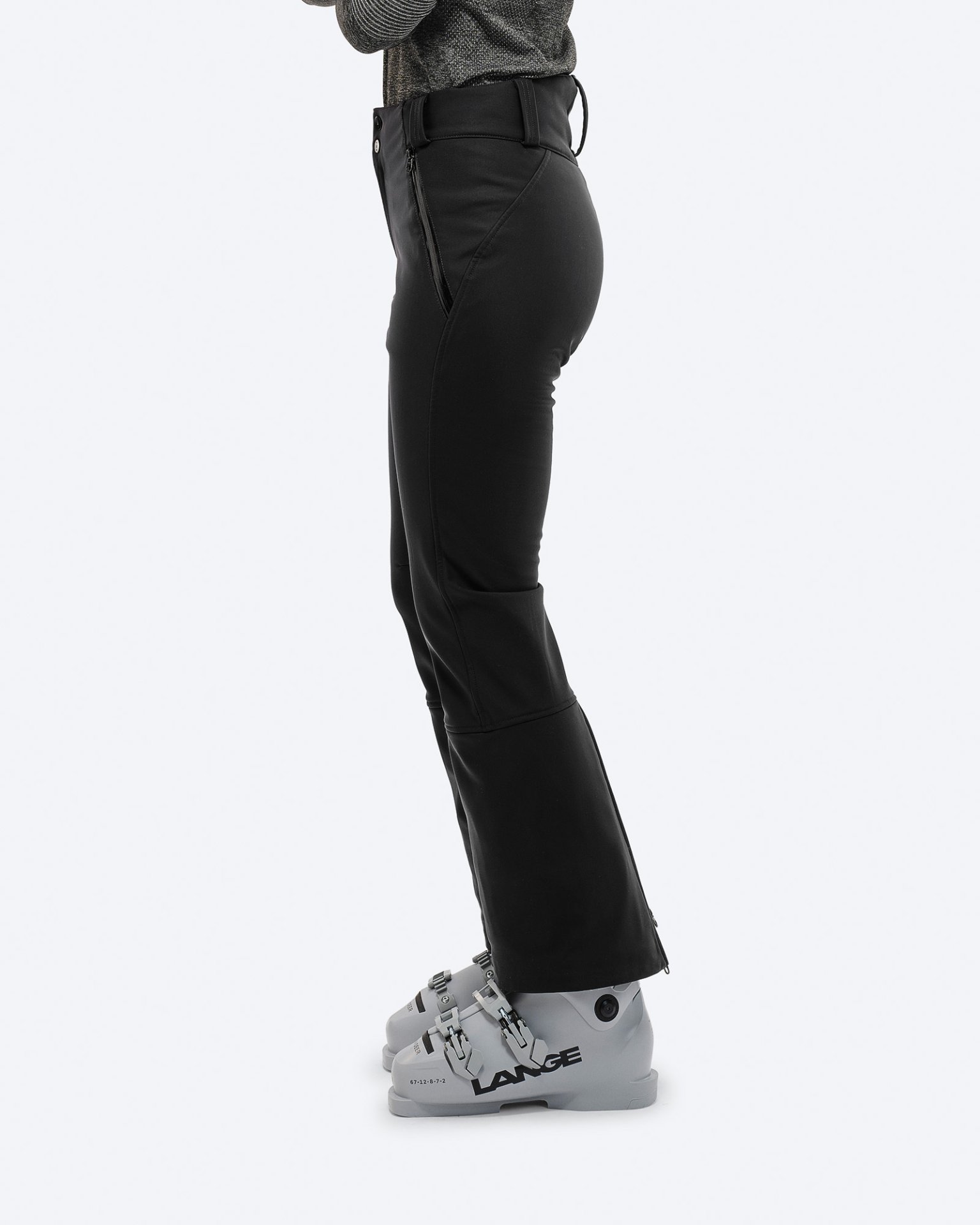 Profilansicht: Schwarze Stretch-Skihose mit Skischuhen. Reißverschlussdetail am Bein.