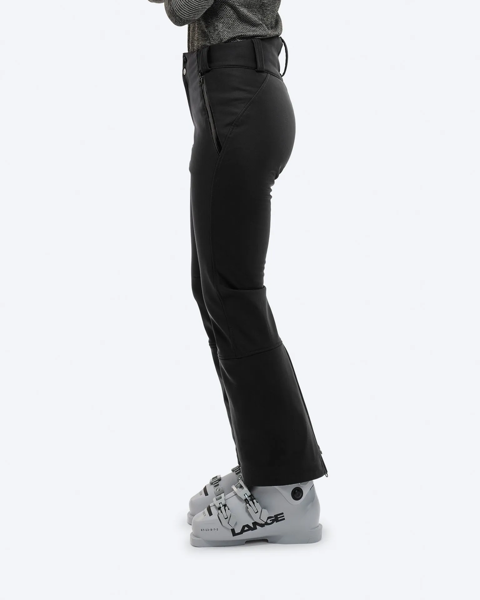 Profilansicht: Schwarze Stretch-Skihose mit Skischuhen. Reißverschlussdetail am Bein.