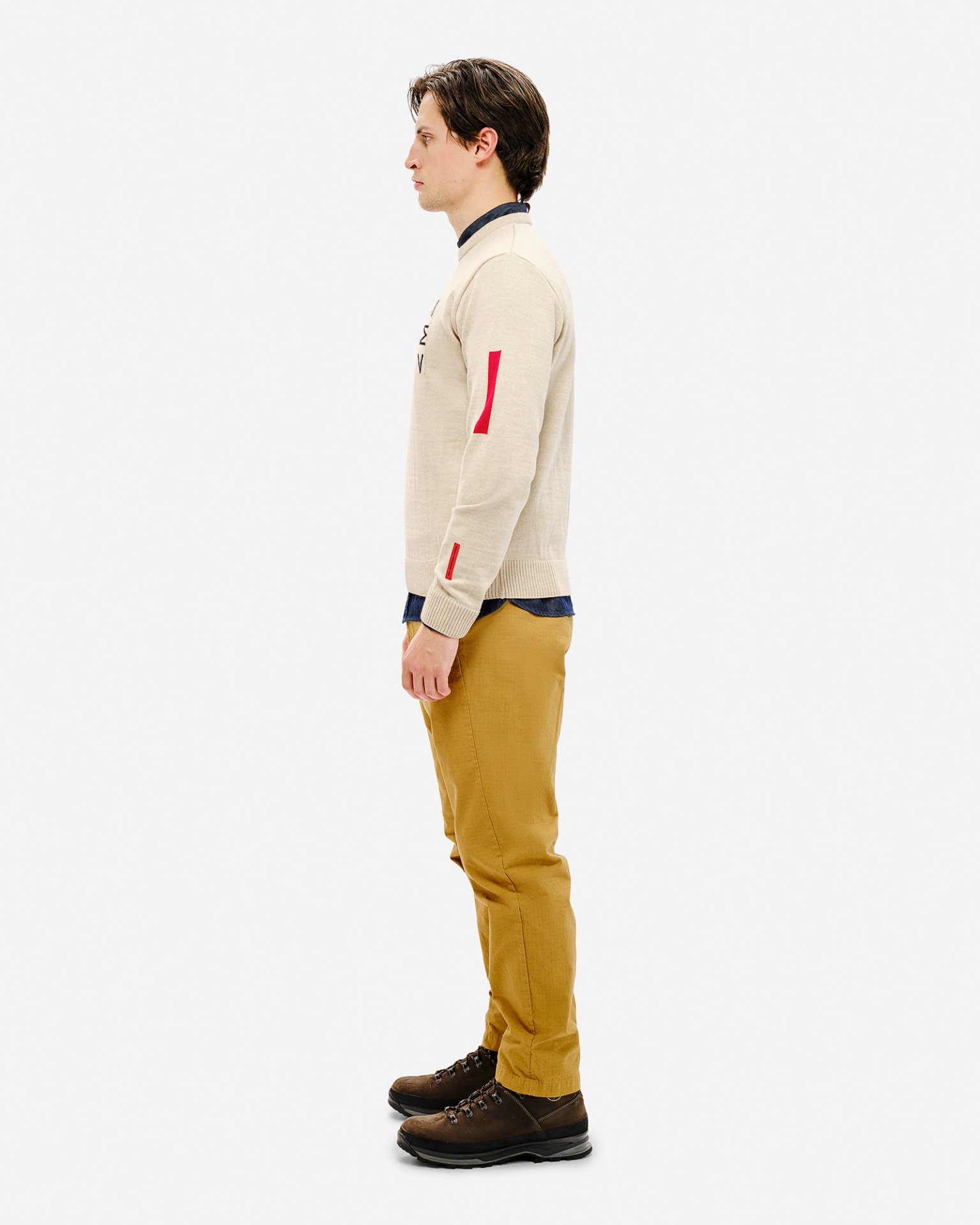 Mann im Profil mit Ski Sweater St. Moritz, beiger Pullover mit roten Details und gelben Hosen.