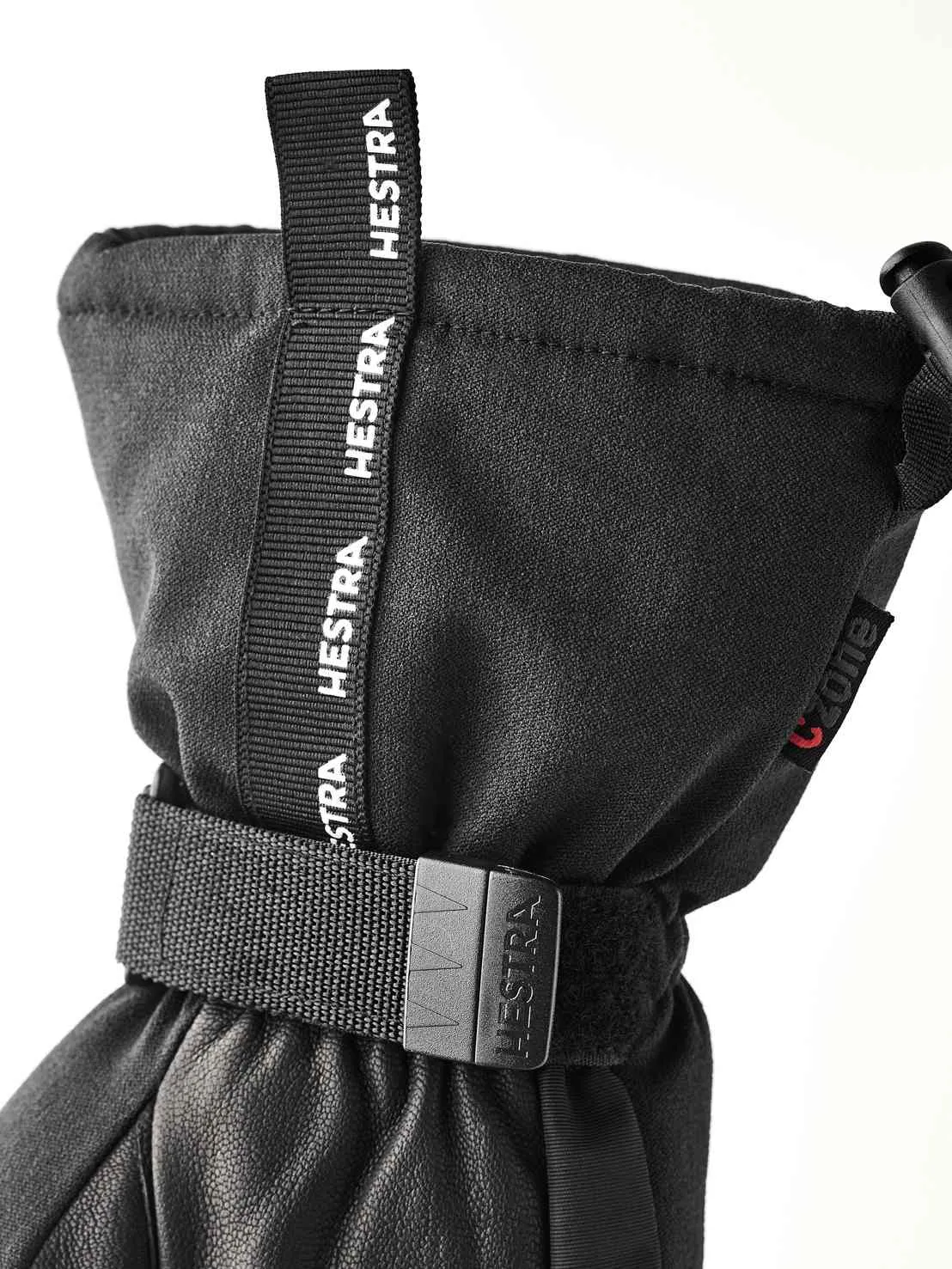 Nahaufnahme eines schwarzen Hestra-Handschuhs mit Zugband und verstellbarem Riemen.