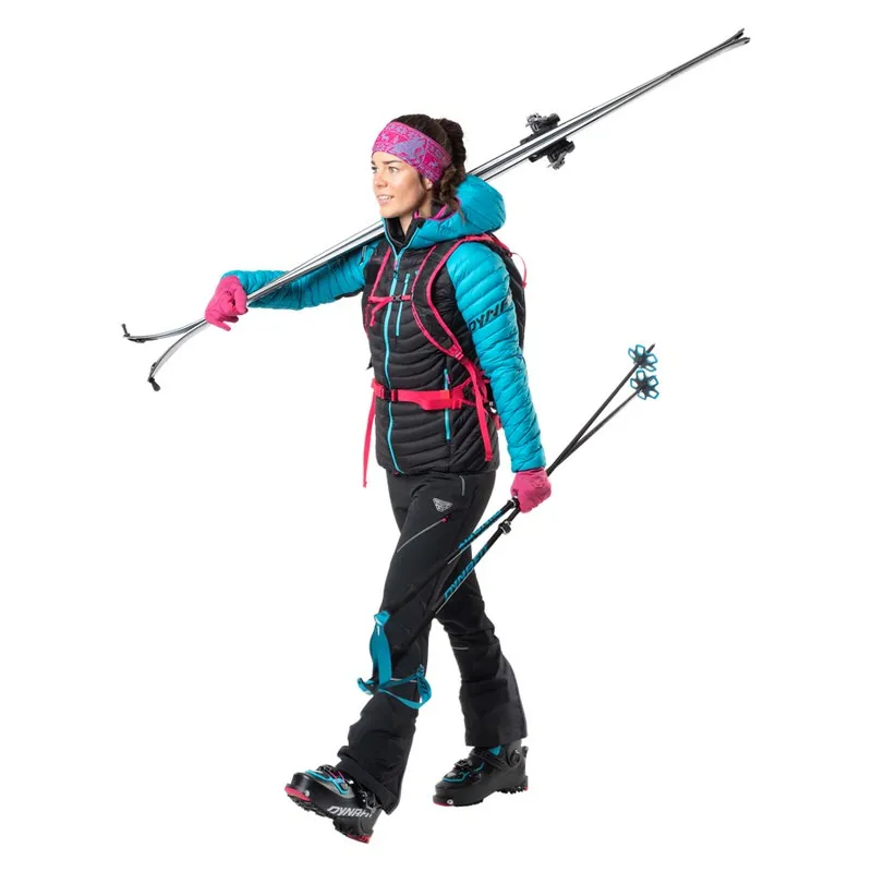 Frau in Skikleidung mit Skiern und Stöcken. Sie trägt eine Dynafit Radical Down RDS Damen Kapuzenjacke in Ocean-Farbe.