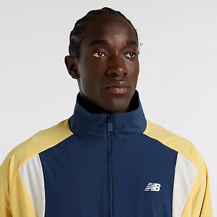 Nahaufnahme einer New Balance Track Jacket in Navy, Gelb und Weiß mit Reißverschluss und NB-Logo.