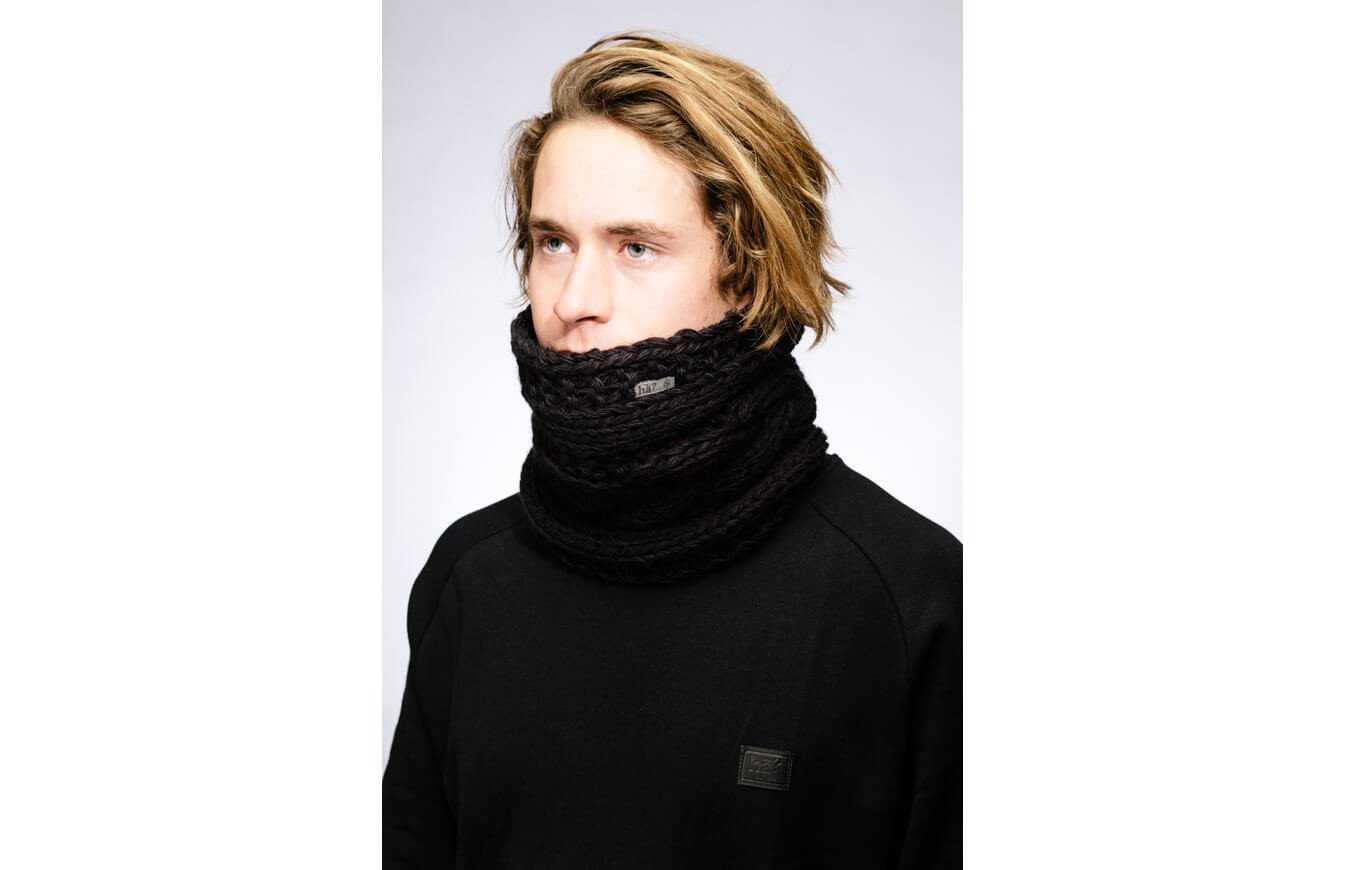 Mann mit blonden Haaren trägt schwarzen, gestrickten Stroller Neckwarmer. Logo-Patch am Hals und Pullover.