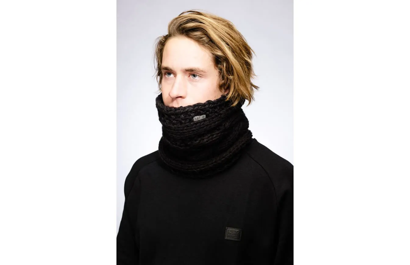 Mann mit blonden Haaren trägt schwarzen, gestrickten Stroller Neckwarmer. Logo-Patch am Hals und Pullover.