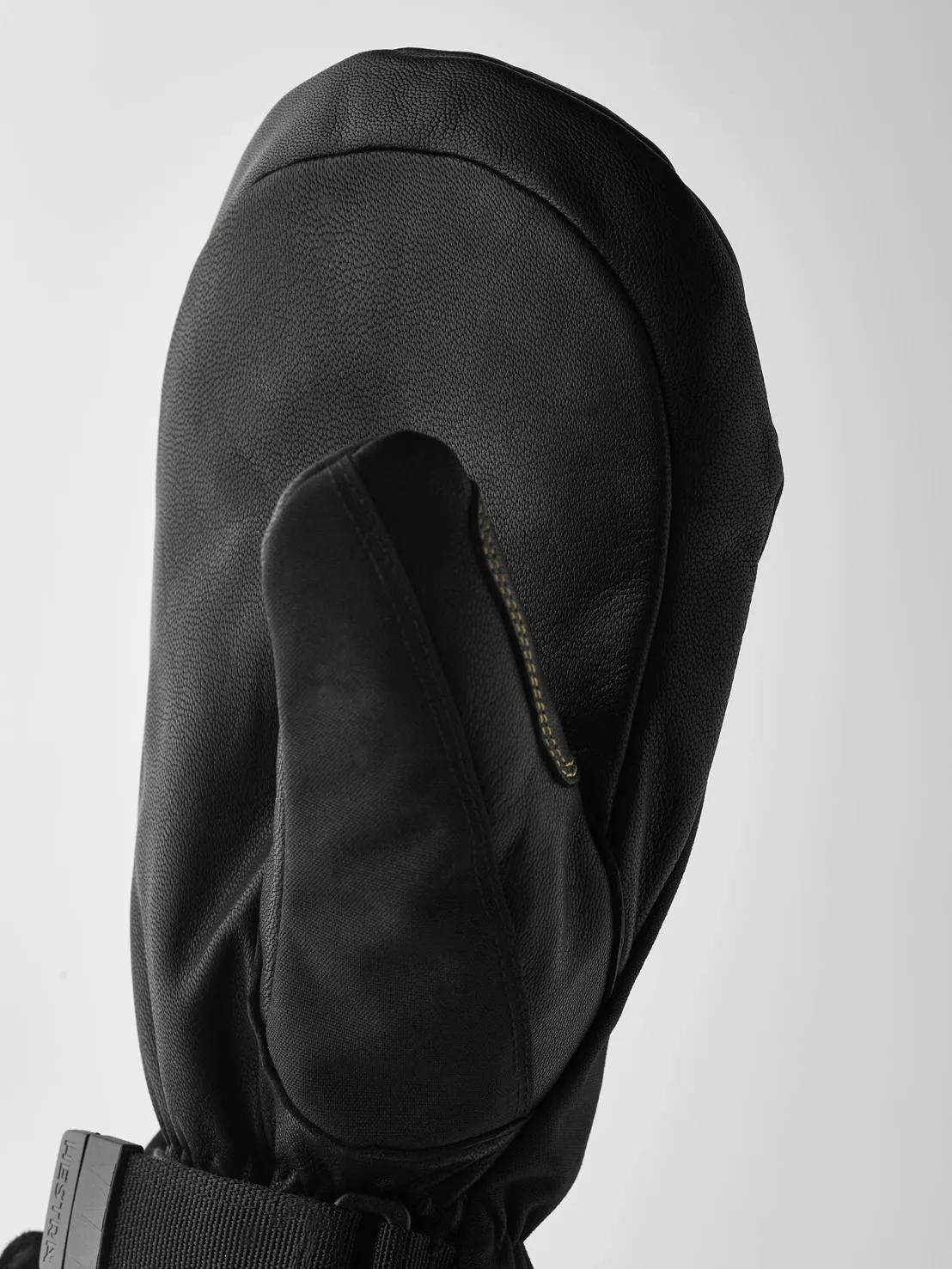 Detailaufnahme eines schwarzen Lederhandschuhs mit Daumen, Manschette mit Band und Schnalle vor hellem Hintergrund.