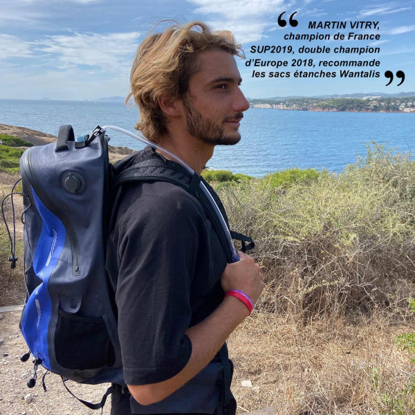 Wasserdichter Rucksack am Meer Mann mit wasserdichtem 35L Rucksack mit Trinksystem vor Küstenlandschaft. Zitat von Martin Vitry im Hintergrund.