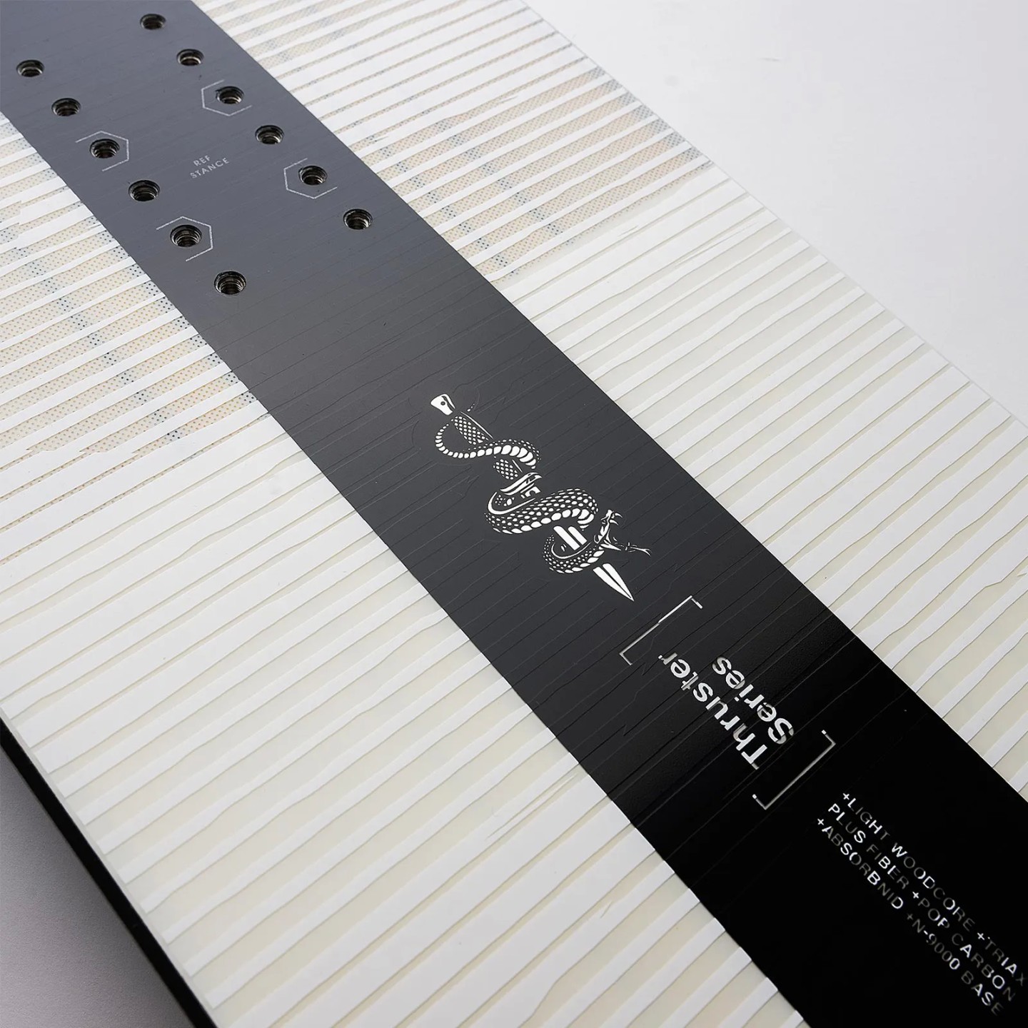 Detailansicht Nidecker Thruster Snowboard: Bindungslöcher, Schlangengrafik auf schwarz-weiß gemustertem Board.