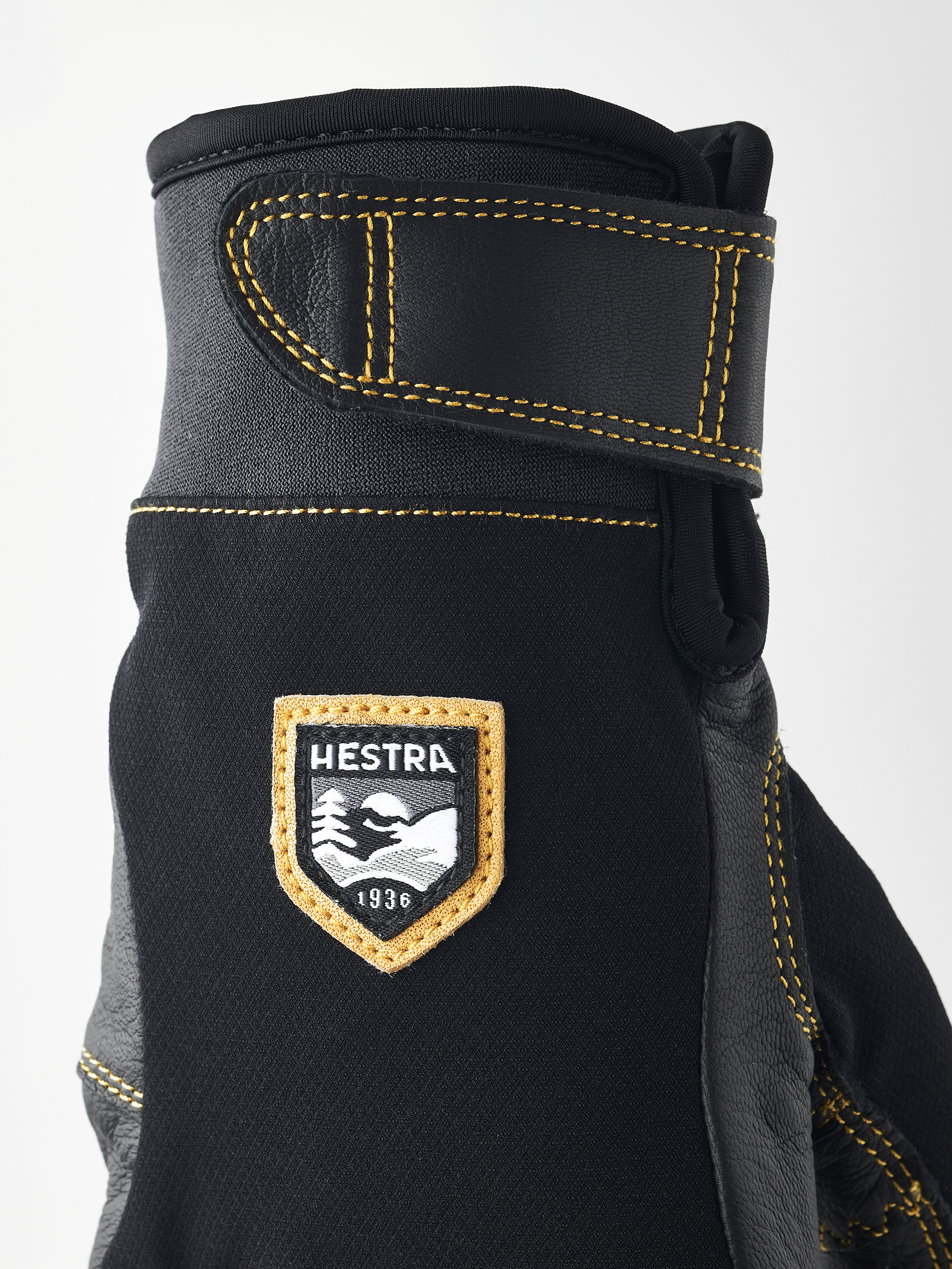 Detailaufnahme eines schwarzen Hestra Ergo Grip Active Handschuhs mit gelben Nähten und Markenlogo.