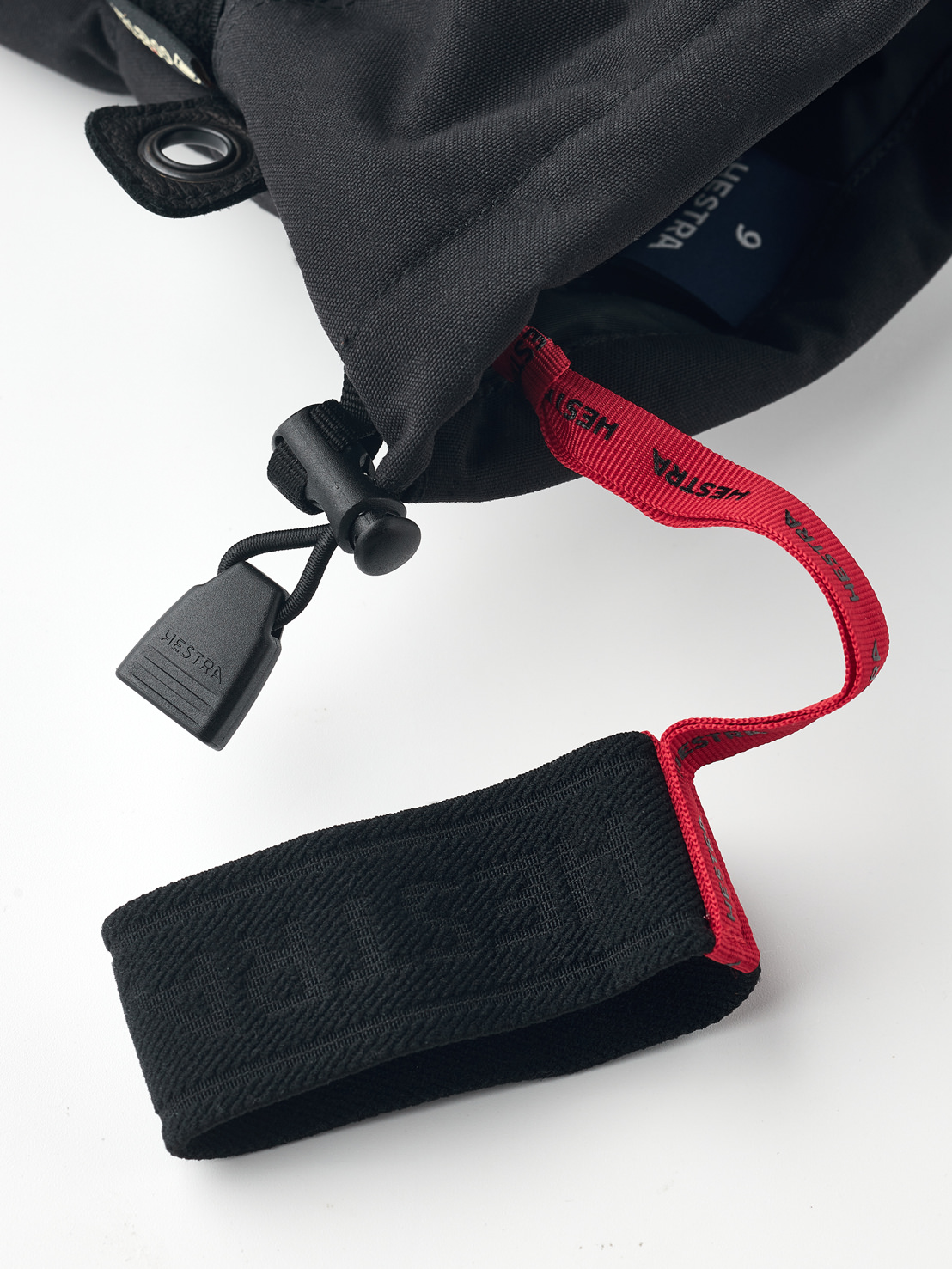 Detailaufnahme eines schwarzen Hestra Gore-Tex Fünffinger-Handschuhs mit roter Schlaufe und schwarzem Verschluss.