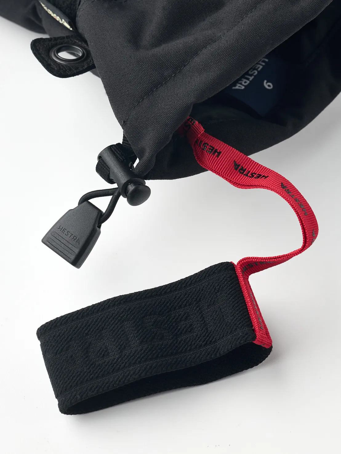 Detailaufnahme eines schwarzen Hestra Gore-Tex Fünffinger-Handschuhs mit roter Schlaufe und schwarzem Verschluss.