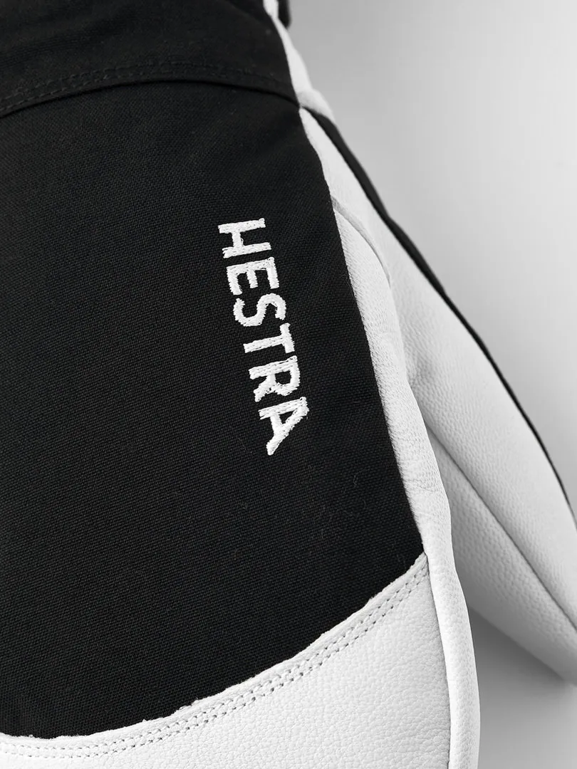 Nahaufnahme eines schwarzen Hestra-Handschuhs mit weißem Leder und dem weißen Schriftzug "HESTRA" auf der Oberseite.