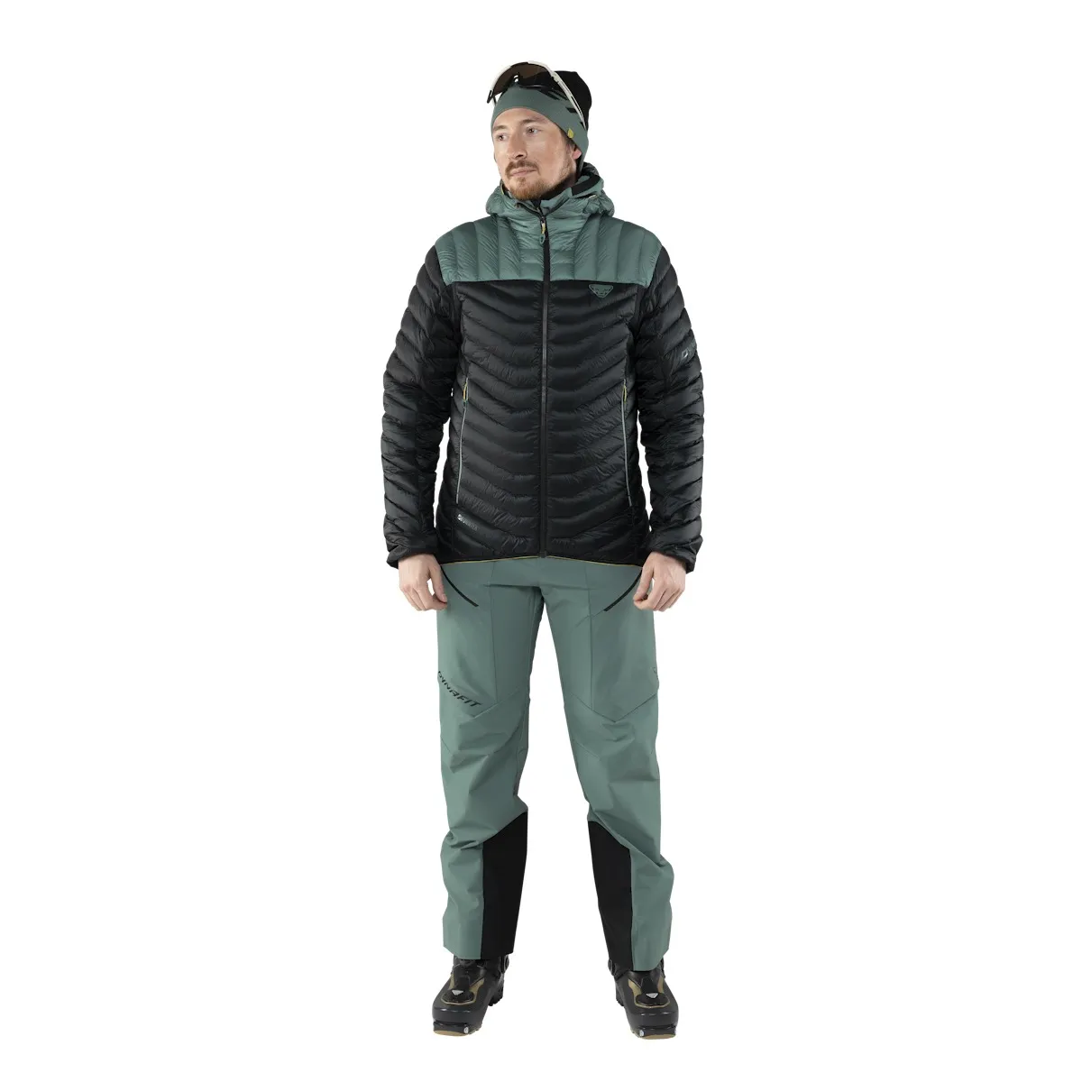 Mann in Daunenjacke und Skitourenhose, vor weißem Hintergrund. Die Jacke ist schwarz und grün.