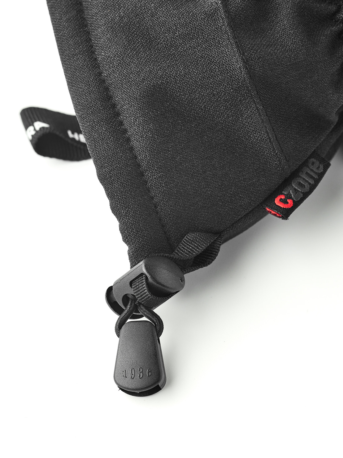 Schwarze Handschuhmanschette 1936 Nahaufnahme einer schwarzen Handschuhmanschette mit Kordelzug, Stopper und '1936' Anhänger. Ein rotes 'Czone' Etikett ist sichtbar.