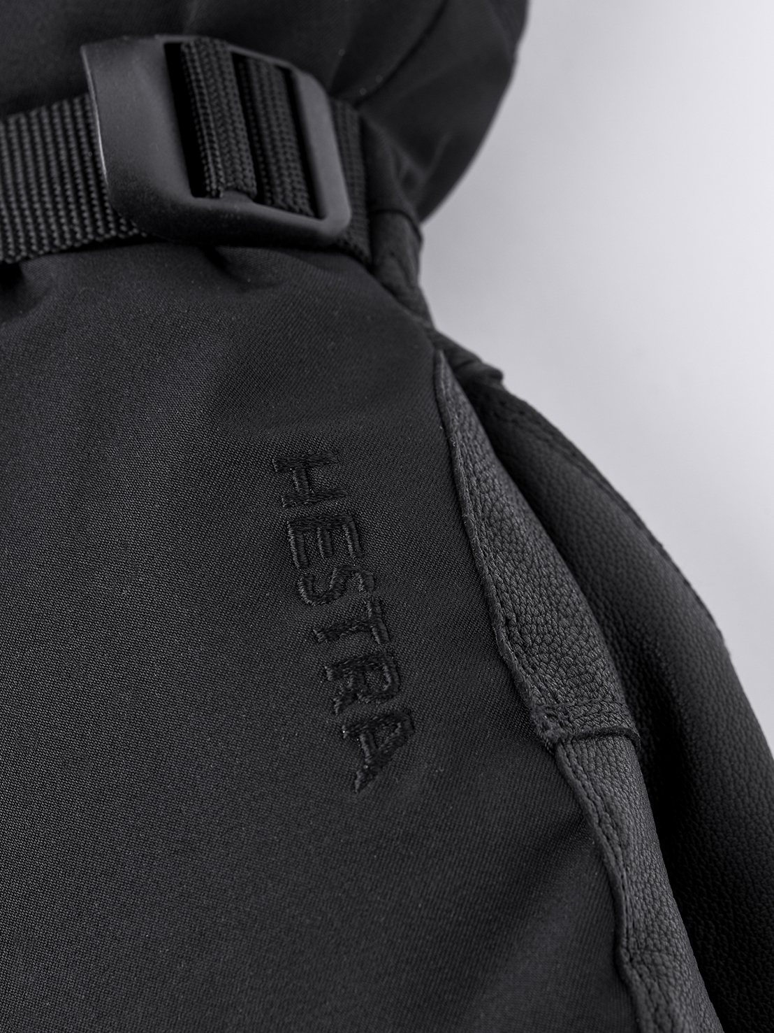 Hestra Army Leather Extreme Detailansicht des schwarzen Hestra Army Leather Extreme Mitt mit Logo und Riemen.