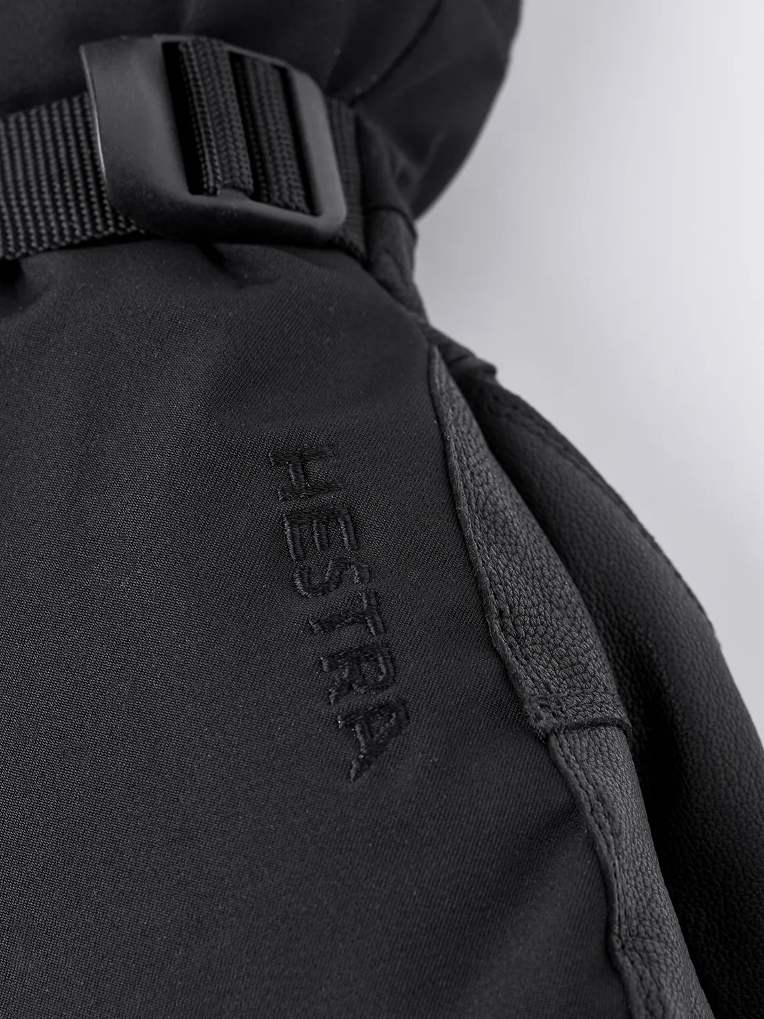 Detailansicht des schwarzen Hestra Army Leather Extreme Mitt mit Logo und Riemen.