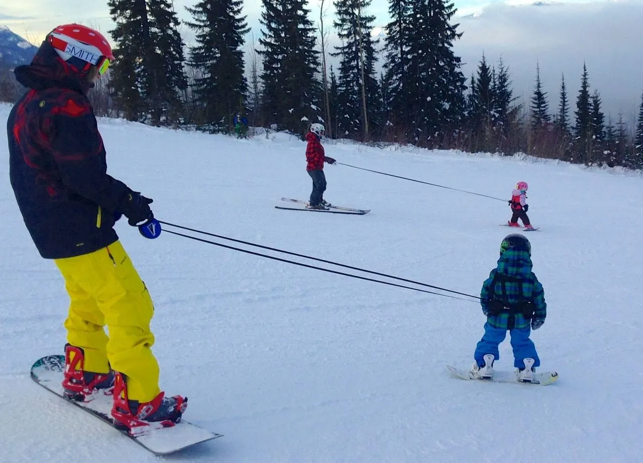 Auf Schnee: Erwachsener Snowboarder mit Lil' Ripper Gripper Leinen, die Kinder beim Skifahren lernen unterstützen.
