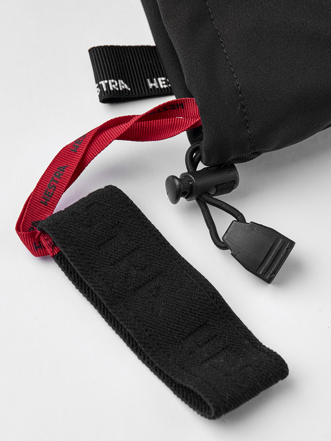 Detailansicht eines schwarzen Hestra Army Leather Extreme Mitt, mit Kordelzug und roter Schlaufe.