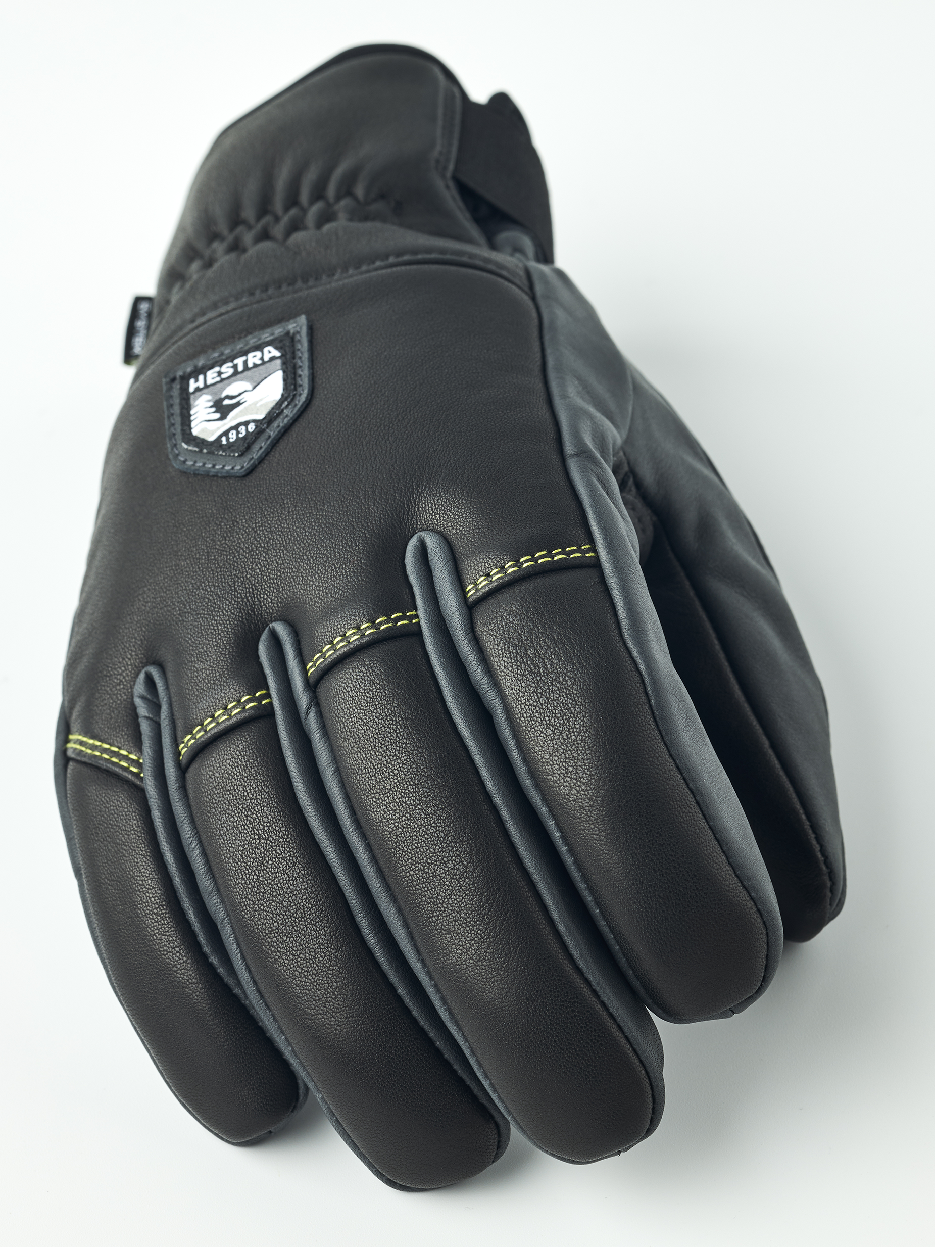 Schwarze Hestra Omni Trigger Handschuhe Detailansicht des schwarzen Hestra Omni Trigger Handschuhs aus Leder mit Logo-Aufnäher und gelber Naht.