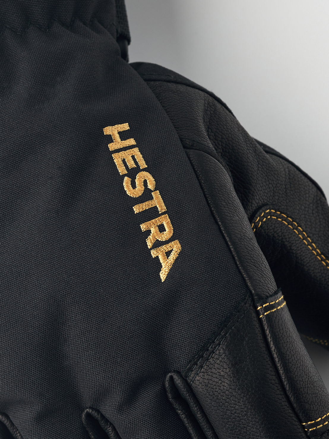 Nahaufnahme eines schwarzen Hestra Gore-Tex Fünffinger-Handschuhs mit goldfarbenem Hestra-Logo.