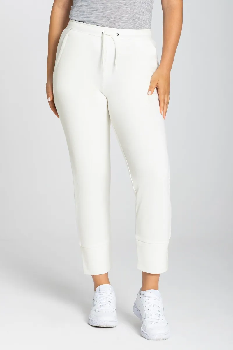 Eine Person trägt eine Super.Natural W Knit Pant in Fresh White, kombiniert mit weißen Sneakers.