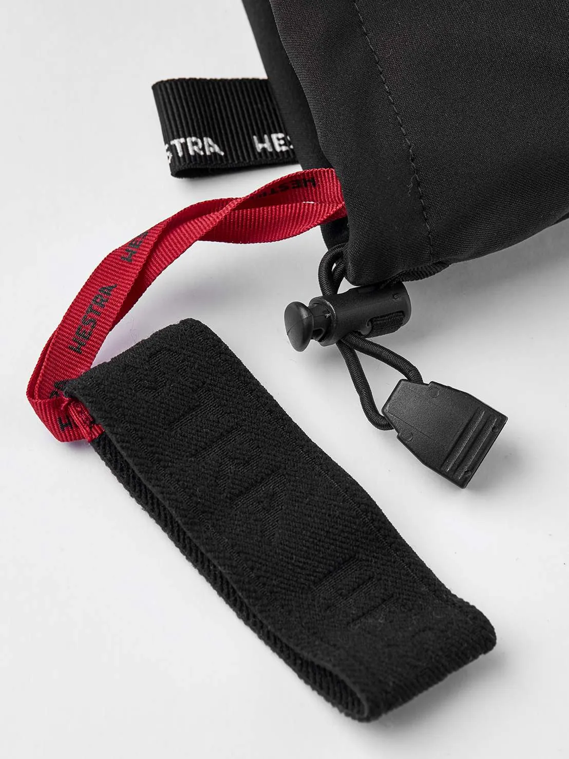Detailansicht eines schwarzen Hestra Army Leather Extreme Mitt, mit Kordelzug und roter Schlaufe.