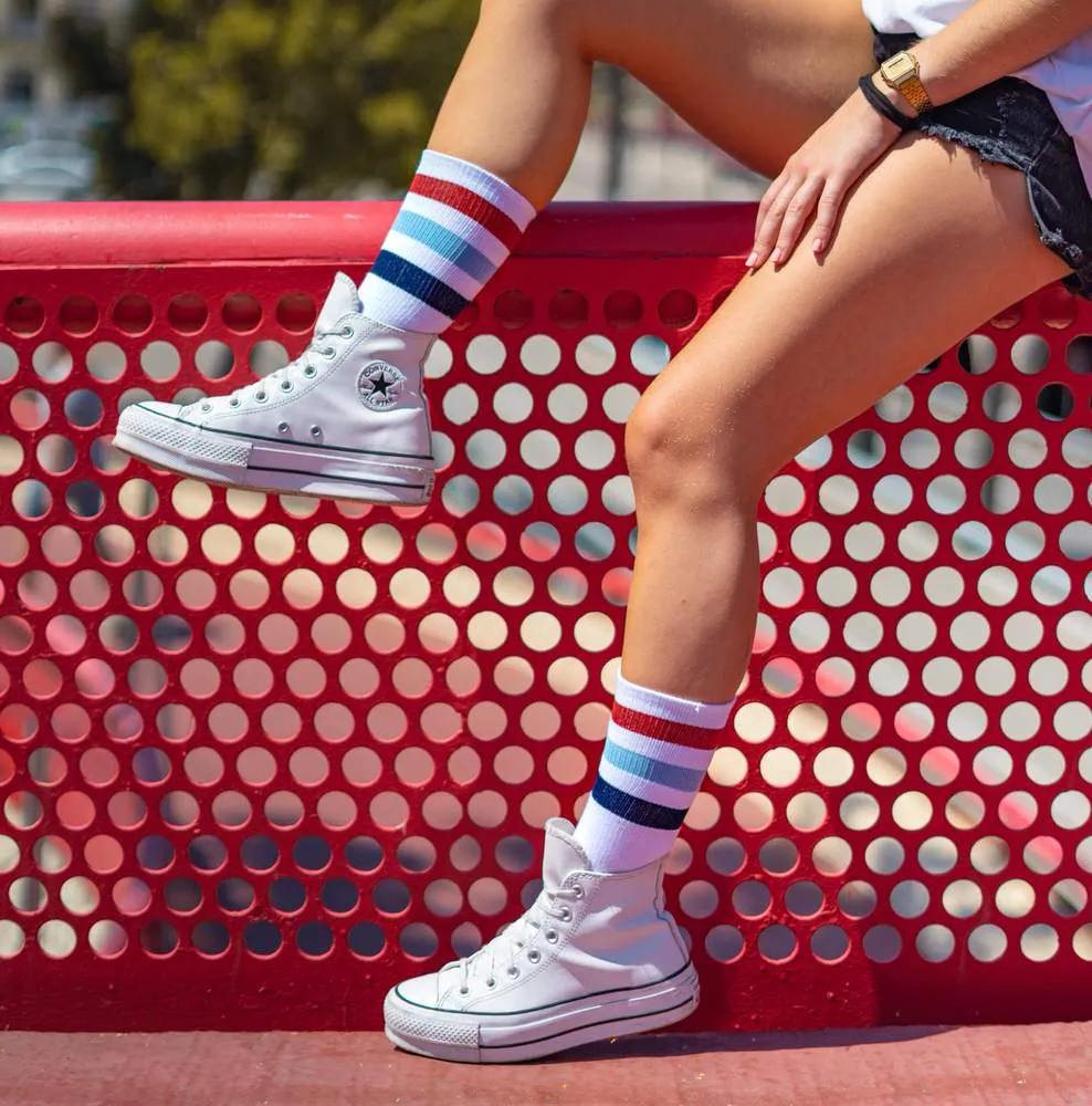 Person mit McFly II Mid High Socken und weißen Schuhen vor rotem Hintergrund.