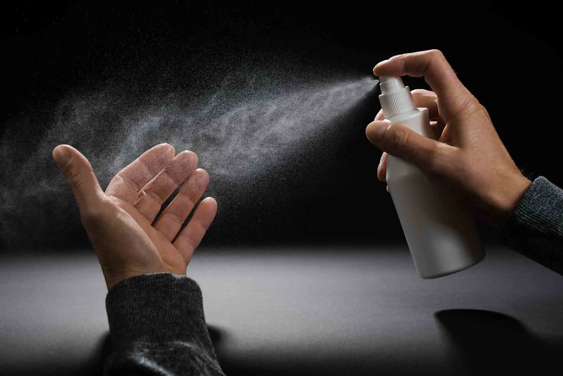 Eine Hand sprüht Desinfektionsmittel aus einer weißen Flasche in eine andere geöffnete Hand.