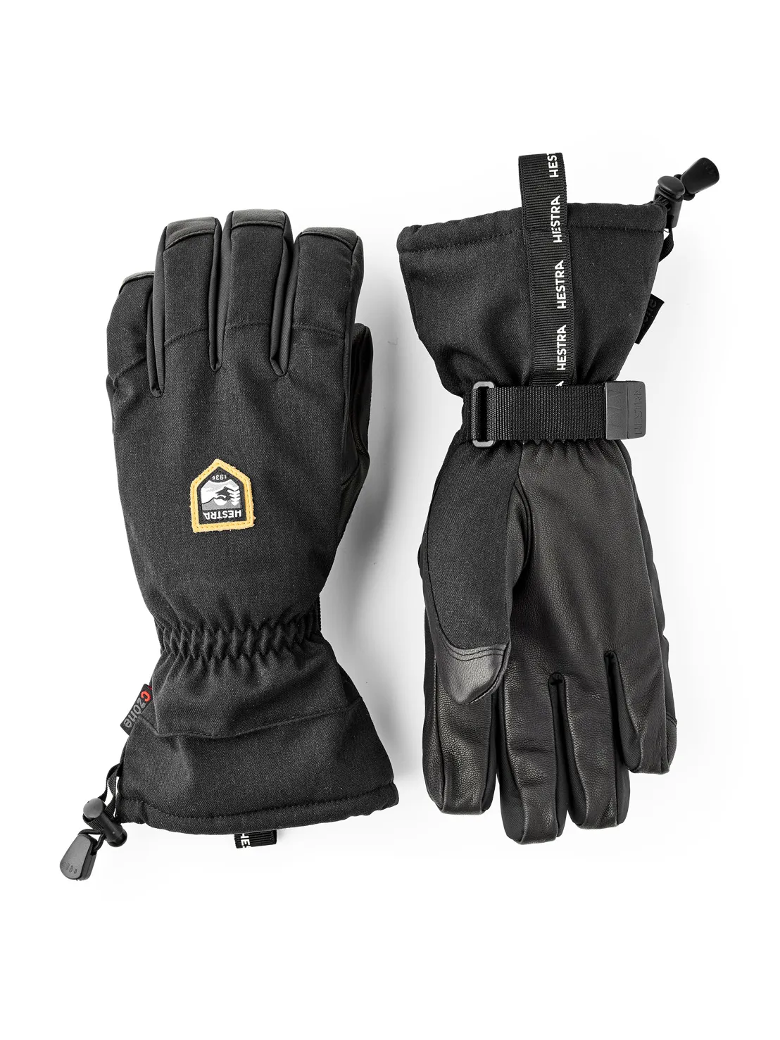 Zwei schwarze Hestra-Handschuhe, einer mit Stoffstulpe und Kordelzug, der andere mit Lederhandfläche und Gurtband.