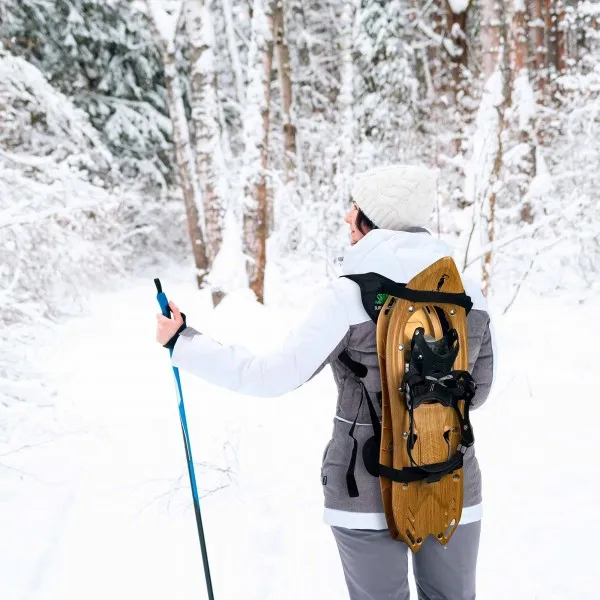 Frau mit Schneeschuhen auf dem Rücken und Skistock im Schnee. Raq Back Rucksack für Schneeschuhe.