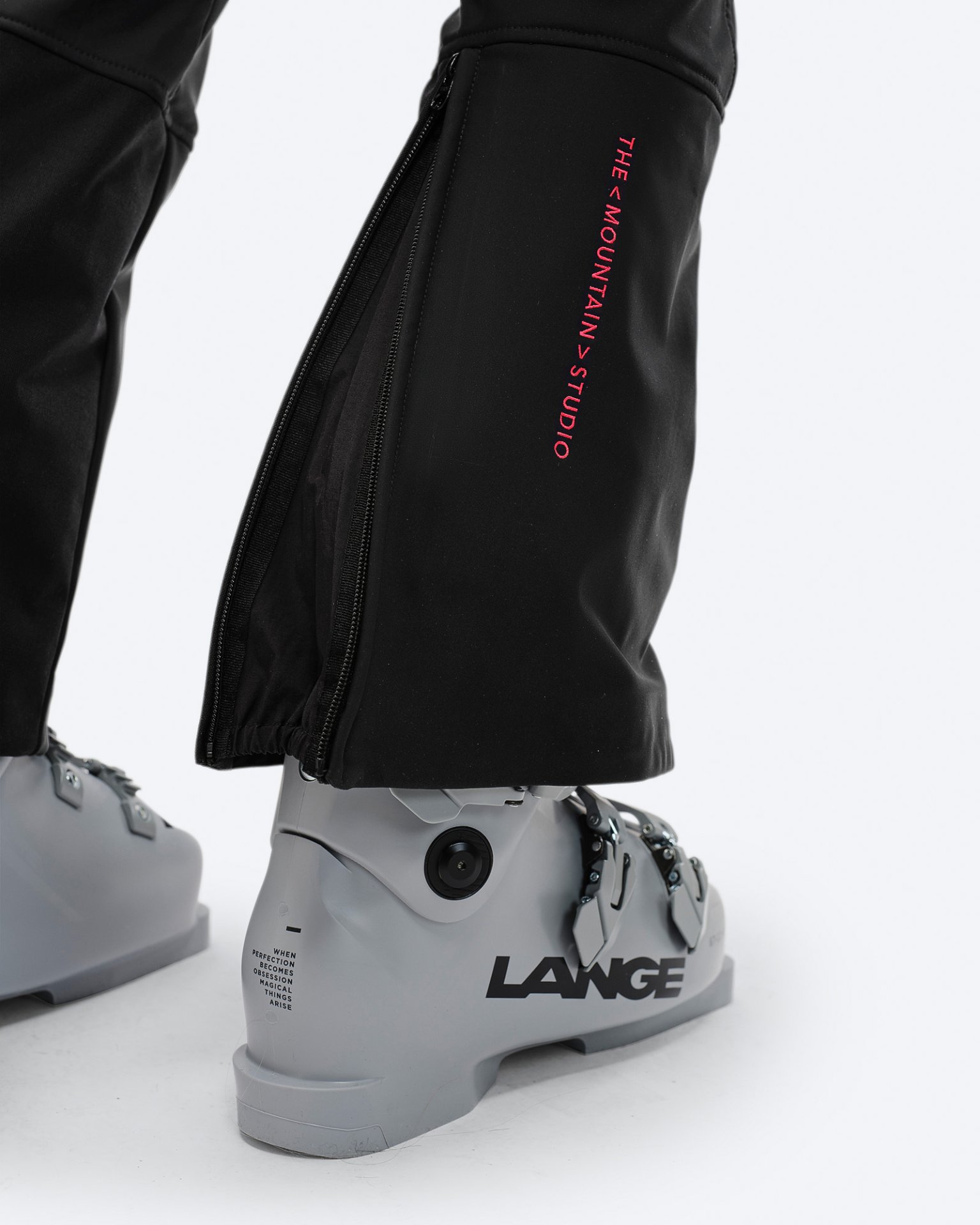 Nahaufnahme einer schwarzen Stretch-Skihose über einem grauen Skischuh mit Reißverschluss und Markenlogo.