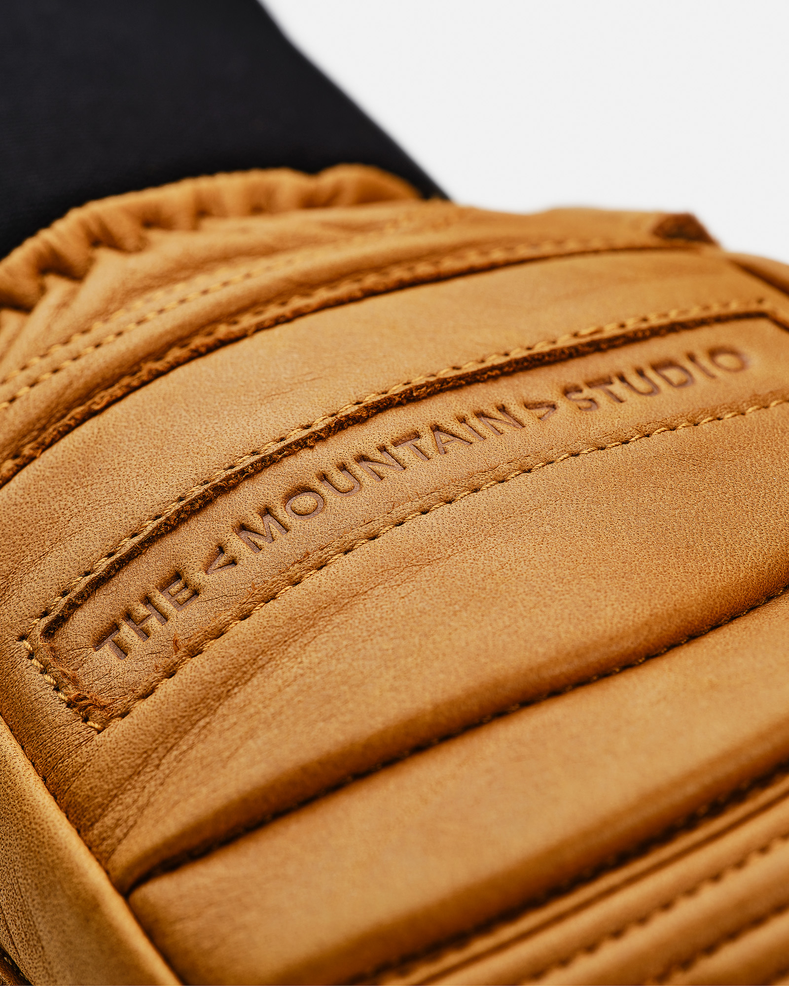 Nahaufnahme eines Lederhandschuhs in Sandfarbe mit "THE MOUNTAINS STUDIO"-Prägung und Steppdetails.