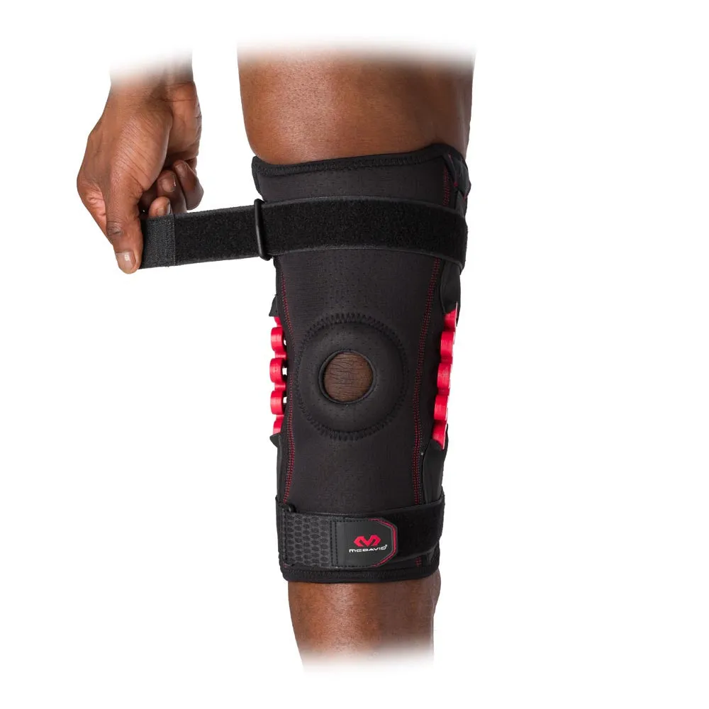 Ein Bein mit angelegter McDavid NRG Knee Brace 30630, die Bandage ist schwarz mit roten Akzenten und wird mit Klettverschluss fixiert.