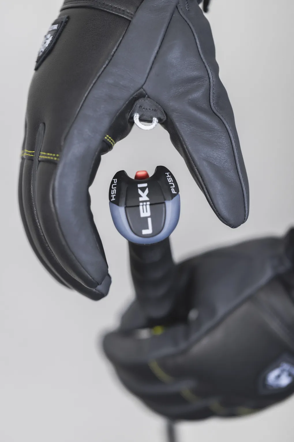 Eine Hand in einem schwarzen Lederhandschuh hält einen Ski Stock mit dem Knopf "LEKI Push".